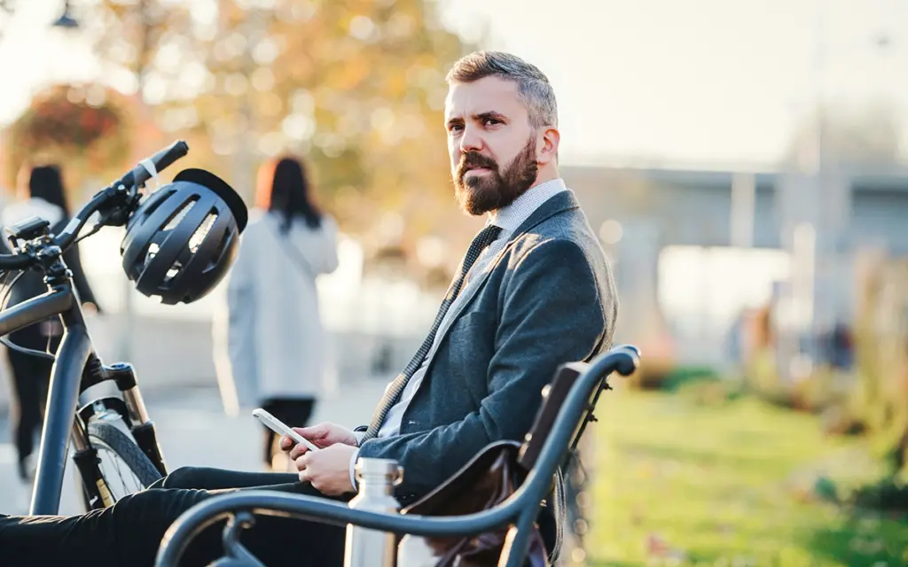 Die besten Hacks gegen langes Sitzen - Rückenschmerzen adé | Geschäftsmann ist mit dem Fahrrad unterwegs und sitzt auf der Bank